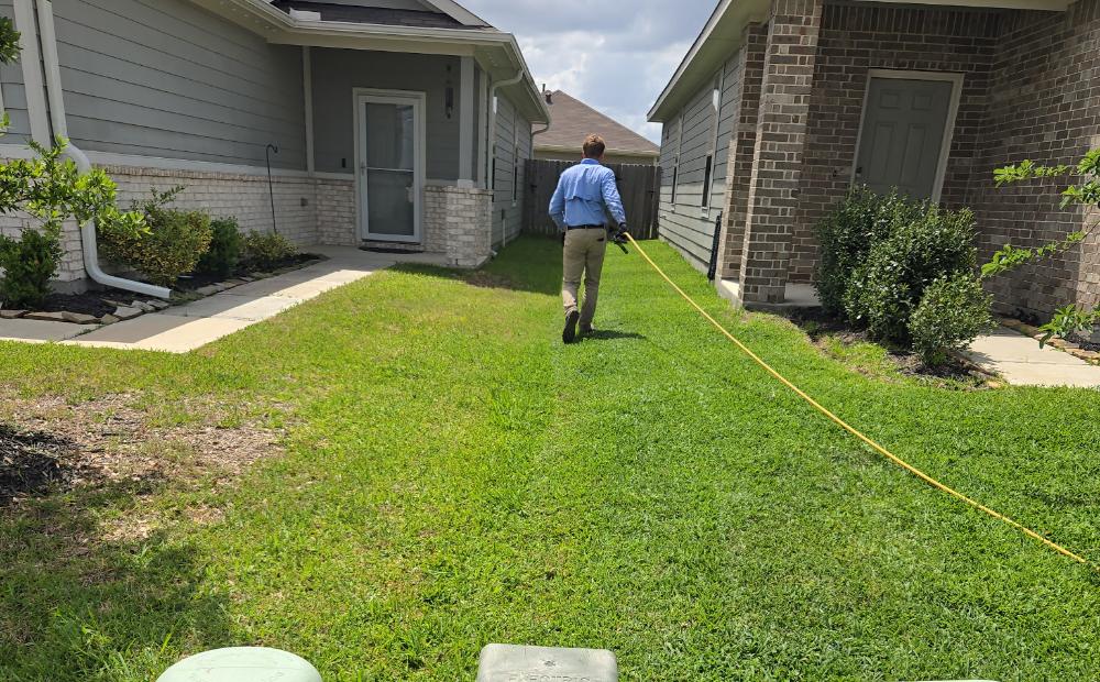 A uniformed Thrive technician pulling a feed line along the side yard of a Houston home